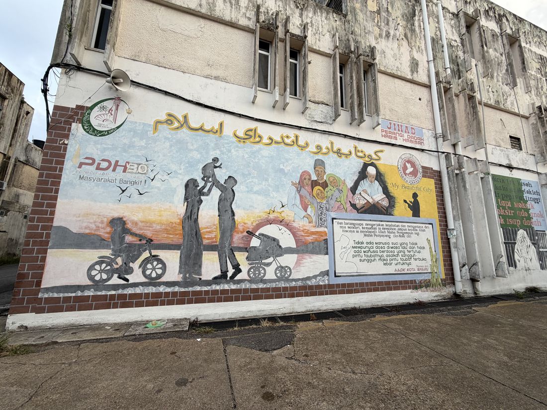 A painted street mural in Kota Bharu showing a family at sunset, Jawi lettering, and an anti-drug campaign panel